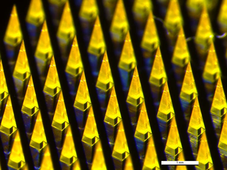 lines of pyramid-shaped microneedles glowing yellow