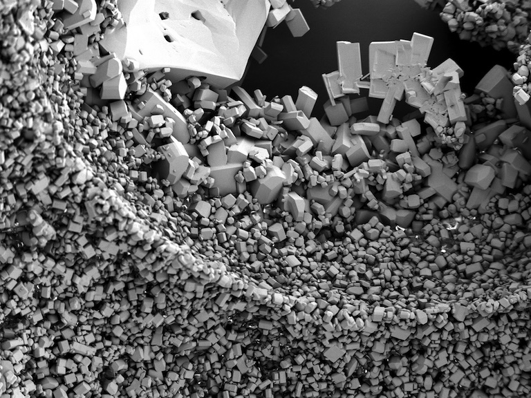 Black and white image of a pile of small square crystals, with bigger crystals loosely arranged across the top. Almost like a seismic wave going through the Earth's crust.